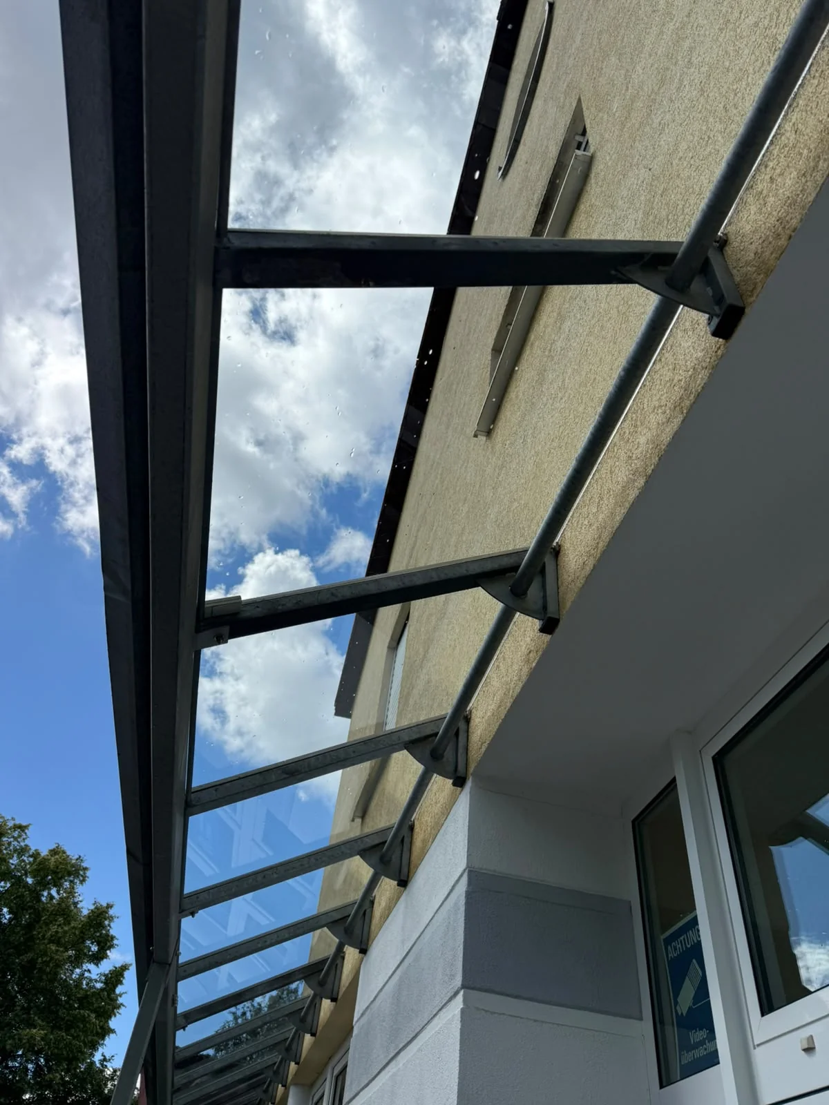 Gereinigtes Glasvordach mit klarer Sicht auf Himmel und Gebäude.